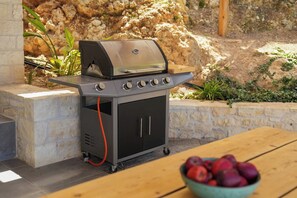 Ein tragbarer Grill mit Bedienfeld und Stauraumschrank, auf einer Steinterrasse mit einem Holztisch und einer Obstschale in der Nähe.