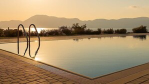 A swimming pool with metal ladders, surrounded by a brick walkway, and a sunset in the background. - Oka Aqua Paradise - Panoramic Seaview with Pool (Drepano)