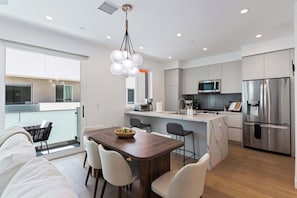A modern kitchen with a central island, stainless steel appliances, and a dining area with a wooden table and chairs.