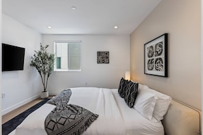 Une chambre à coucher moderne avec un lit, une plante en pot, des œuvres d’art et une fenêtre.