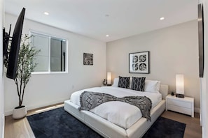 A modern bedroom with a large bed, bedside tables, a TV, and artwork on the walls.