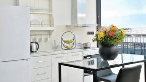 A modern kitchen with white cabinetry, a Bosch refrigerator, a stove, and a dining table with a black vase of flowers.