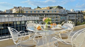 A round table with white metal chairs on a balcony overlooking a cityscape.