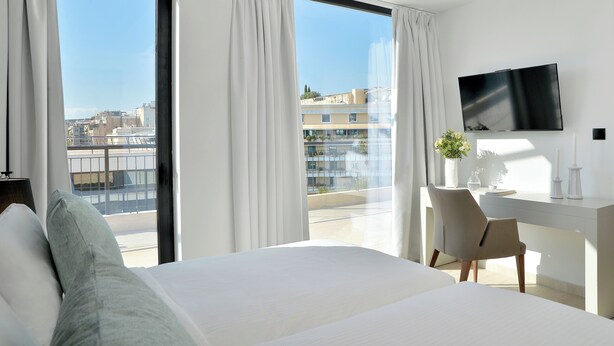 A hotel room with a bed, a desk, a chair, a TV, and large windows with curtains.