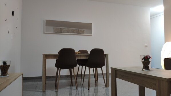 Un comedor con una mesa de madera y cuatro sillas, un florero con una planta y una obra de arte enmarcada en la pared.
