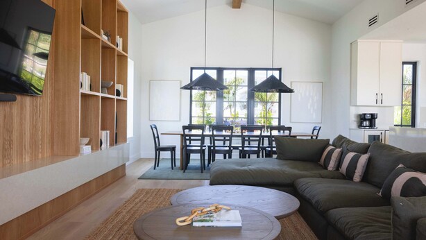 A modern living room with a sectional sofa, a coffee table, and a wooden bookshelf. - The Shellstone House at Solaire Lunara Bay (Key West)