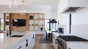 A modern kitchen with a central island, a dining area, and a large window. - The Shellstone House at Solaire Lunara Bay (Key West)