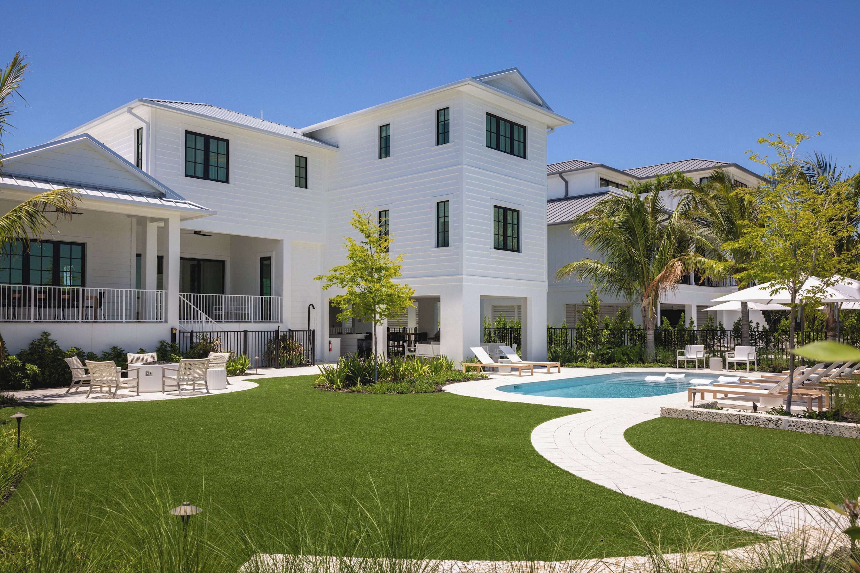A two-story house with a swimming pool, outdoor seating, and a well-maintained lawn.