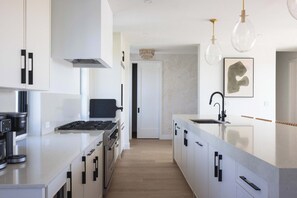 A modern kitchen with white cabinets, a built-in stove, and a large island with a sink.