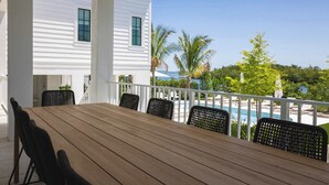 A covered outdoor area with a wooden table and chairs, overlooking a swimming pool and a view of the ocean. - The Shellstone House at Solaire Lunara Bay (Key West)