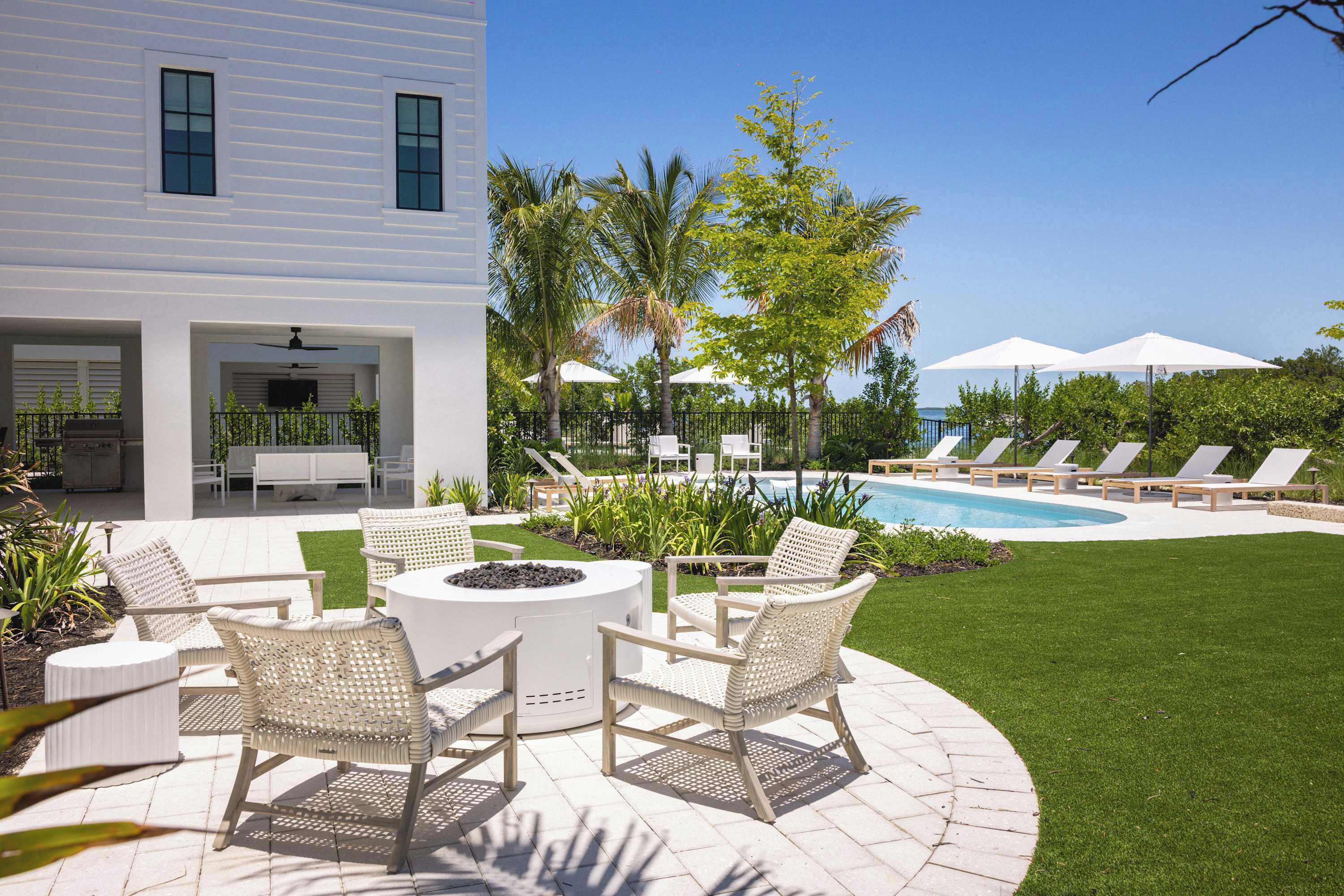 A modern outdoor patio with a pool, lounge chairs, and a fire pit.