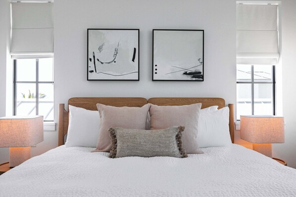 Un lit bien fait, avec une literie blanche et deux oreillers, une tête de lit en bois et deux tableaux abstraits accrochés au mur.