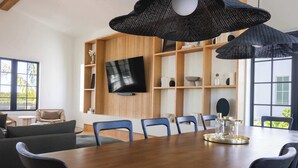 A modern dining area with a wooden table, blue chairs, and a large black woven light fixture. - The Shellstone House at Solaire Lunara Bay (Key West)