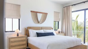 A bedroom with a bed, bedside tables, a wall-mounted light fixture, and a window with curtains. - The Sunray Home at Lunara Bay (Key West)