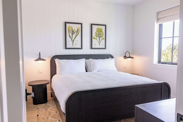 Une chambre à coucher avec un lit, deux lampes fixées au mur, une petite table ronde et une fenêtre donnant sur un paysage agréable.