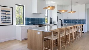 A modern kitchen with a central island, bar stools, and pendant lighting. - The Sunray Home at Lunara Bay (Key West)