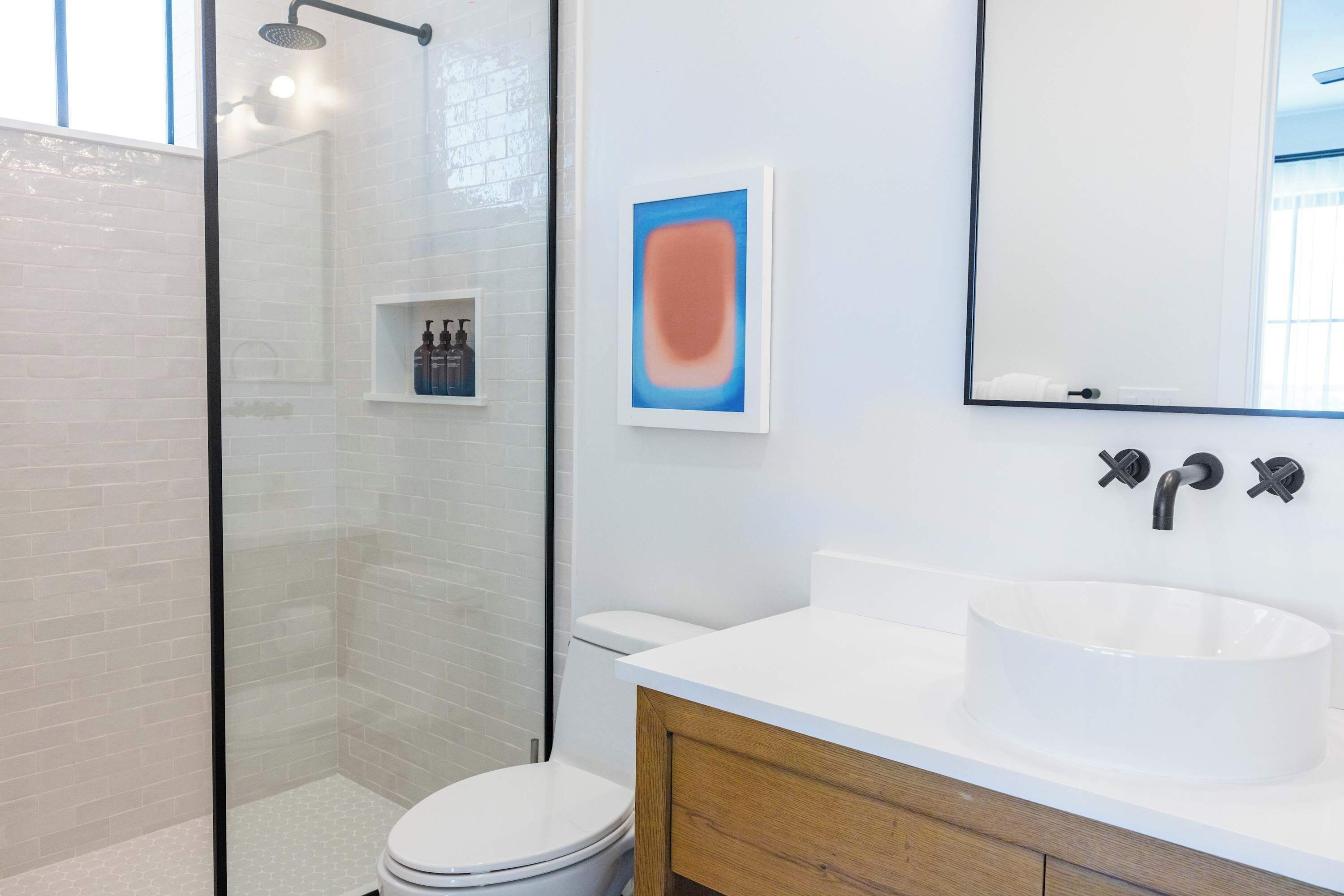 Une salle de bain moderne avec une douche à parois de verre, des toilettes blanches, un lavabo blanc et un meuble-lavabo en bois.
