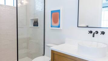 Une salle de bain moderne avec une douche à parois de verre, des toilettes blanches, un lavabo blanc et un meuble-lavabo en bois.