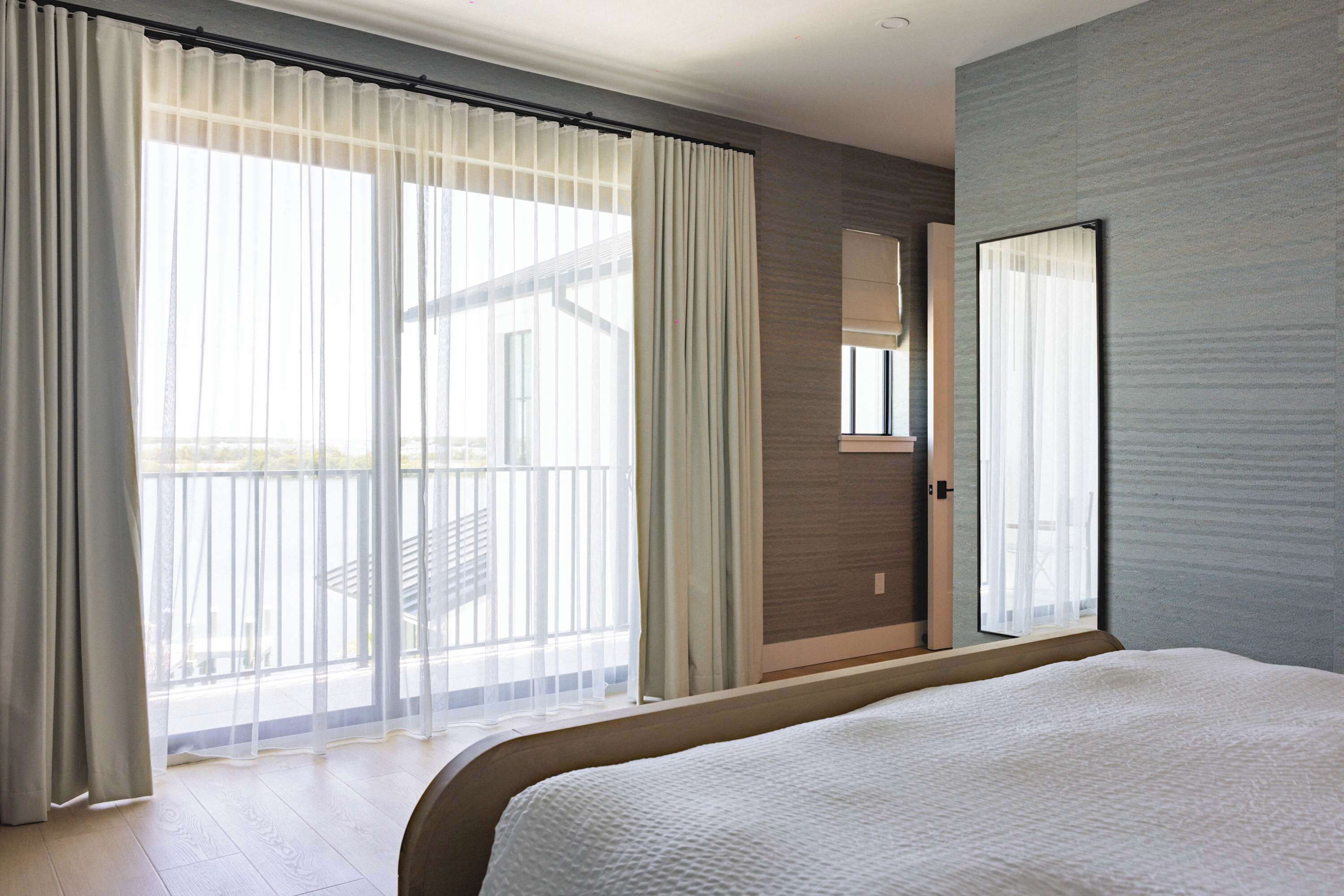 A hotel room with a large bed, a sliding glass door to a balcony, a mirror on the wall, and a wooden floor.