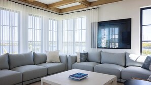 Una sala de estar moderna con un sofá seccional, una mesa de centro y ventanas amplias con cortinas translúcidas.
