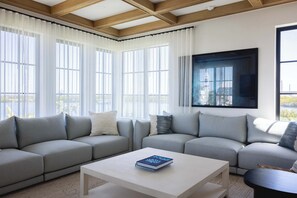 A modern living room with a sectional sofa, a coffee table, and large windows with sheer curtains.