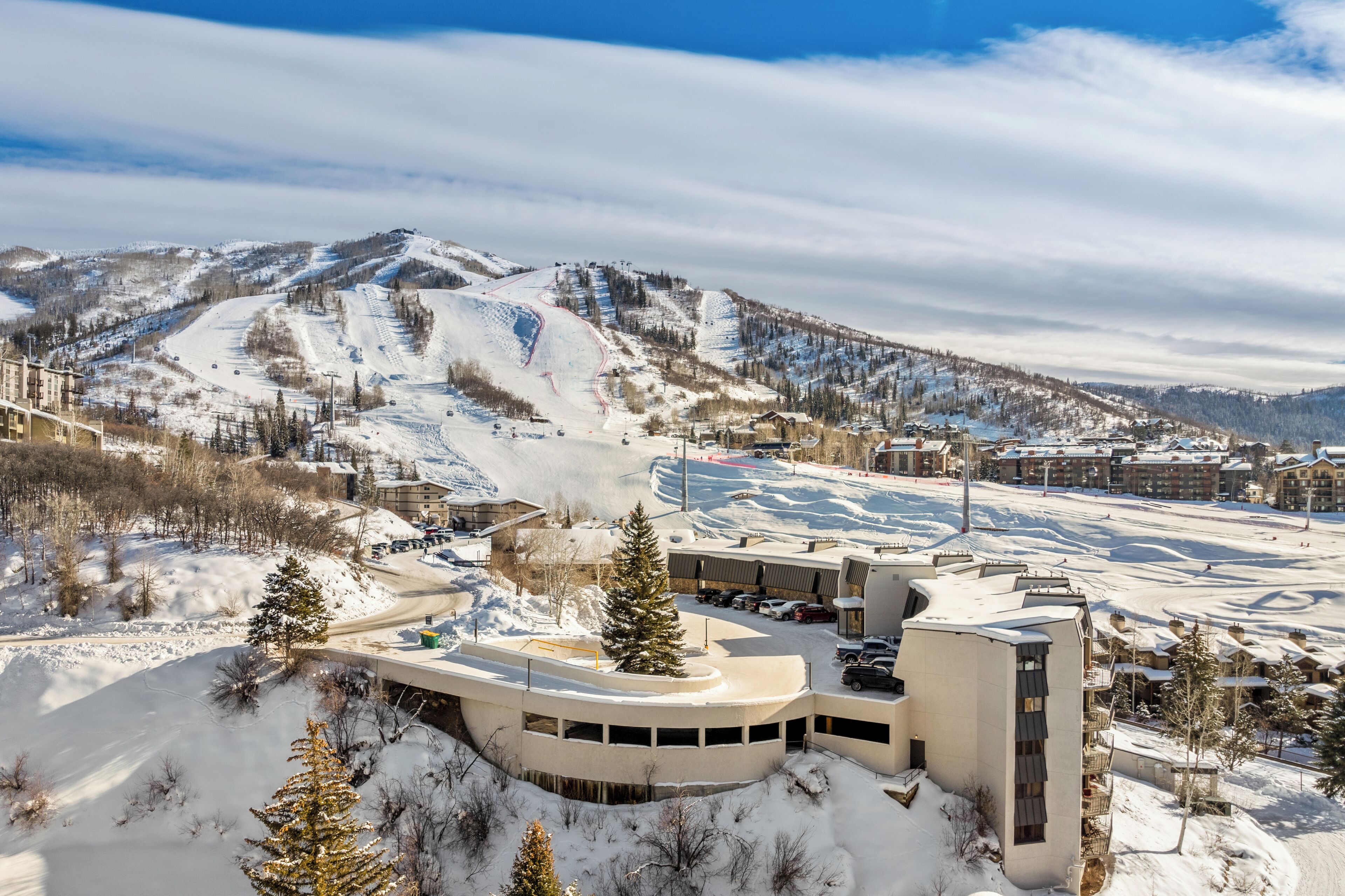 Une station de ski avec un bâtiment aux lignes courbes, des pistes enneigées et un paysage montagneux en toile de fond.