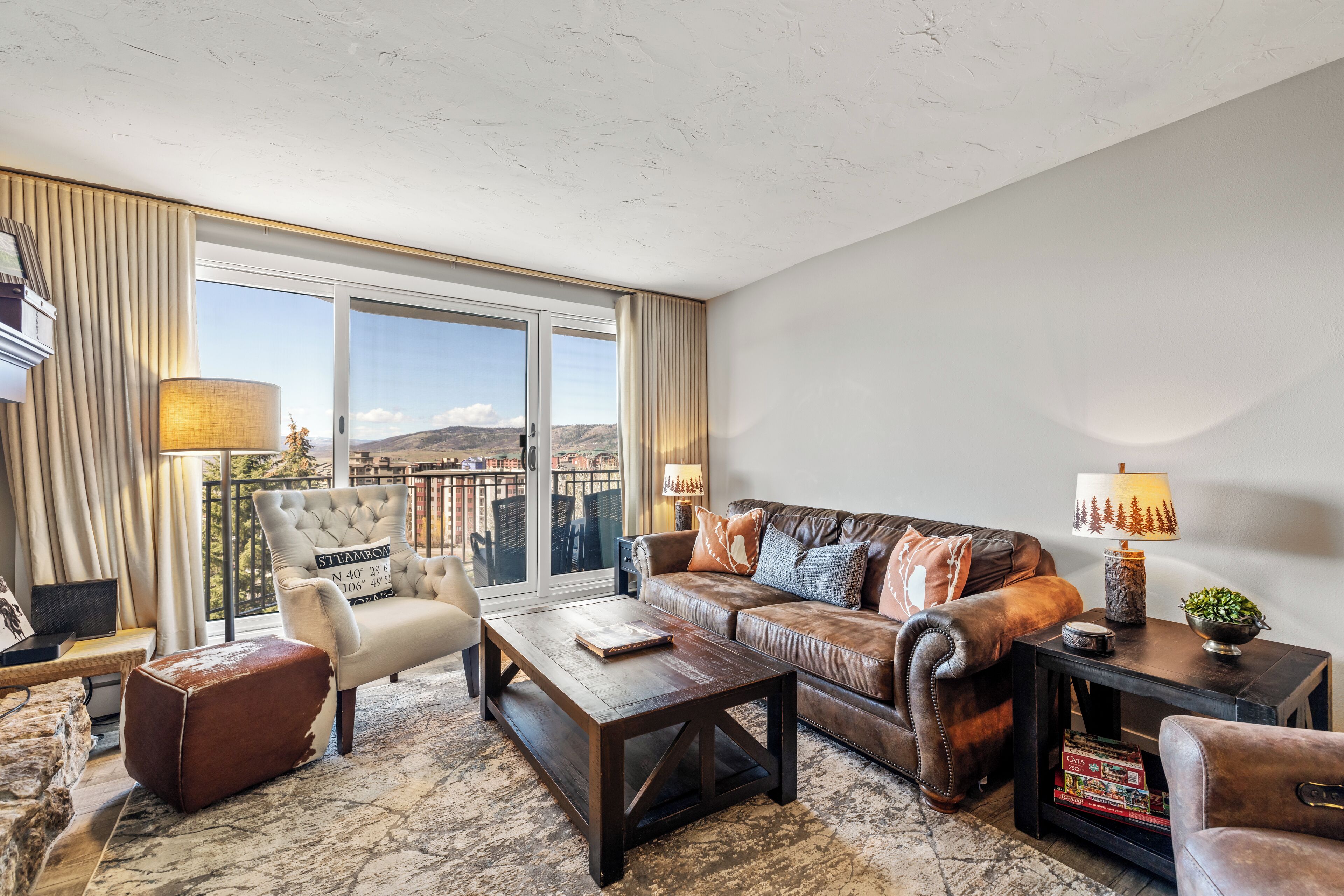 A spacious living room with a large window, leather sofa, armchair, and coffee table.