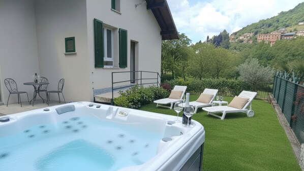 A hot tub with lounge chairs and a table, surrounded by a well-maintained lawn and a building with green shutters. - Ema Home - nature and Lake Como (Argegno)
