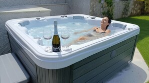 A hot tub with a bottle of champagne and glasses, surrounded by a wooden deck and a stone wall. - Ema Home - nature and Lake Como (Argegno)