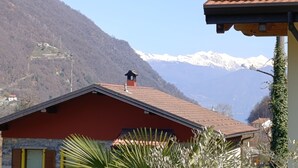A mountain landscape with a red-roofed building in the foreground and snow-capped mountains in the background. - Ema Home - nature and Lake Como (Argegno)