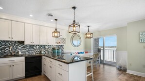 A modern kitchen with white cabinets, a black countertop, and a large island. There are three pendant lights hanging above the island.