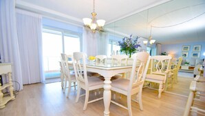 Un espace repas comprenant une table en verre, des chaises blanches, un lustre et un grand miroir.
