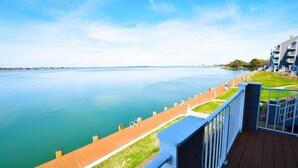 Une vue sur le front de mer depuis un balcon doté d’une terrasse en bois, d’une pelouse et d’une étendue d’eau calme.