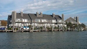 Une propriété située au bord de l’eau, dotée de plusieurs toits à pignons, d’un quai avec des bateaux et d’un ciel dégagé.