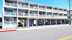 Un motel de varios pisos con balcones, un estacionamiento y un cielo azul despejado.