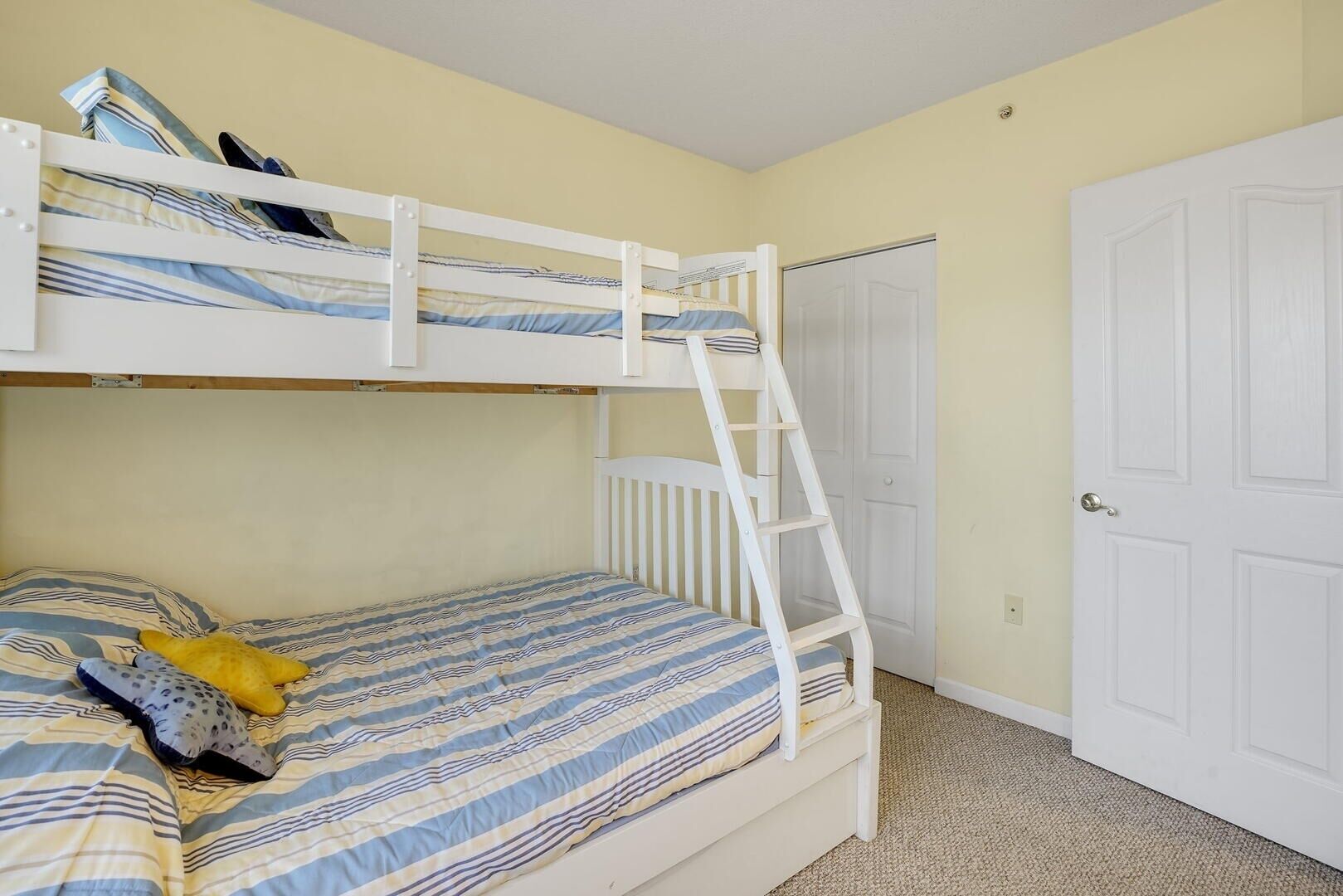 Une chambre avec un lit superposé, une échelle, une porte et une couvre-lit à rayures.