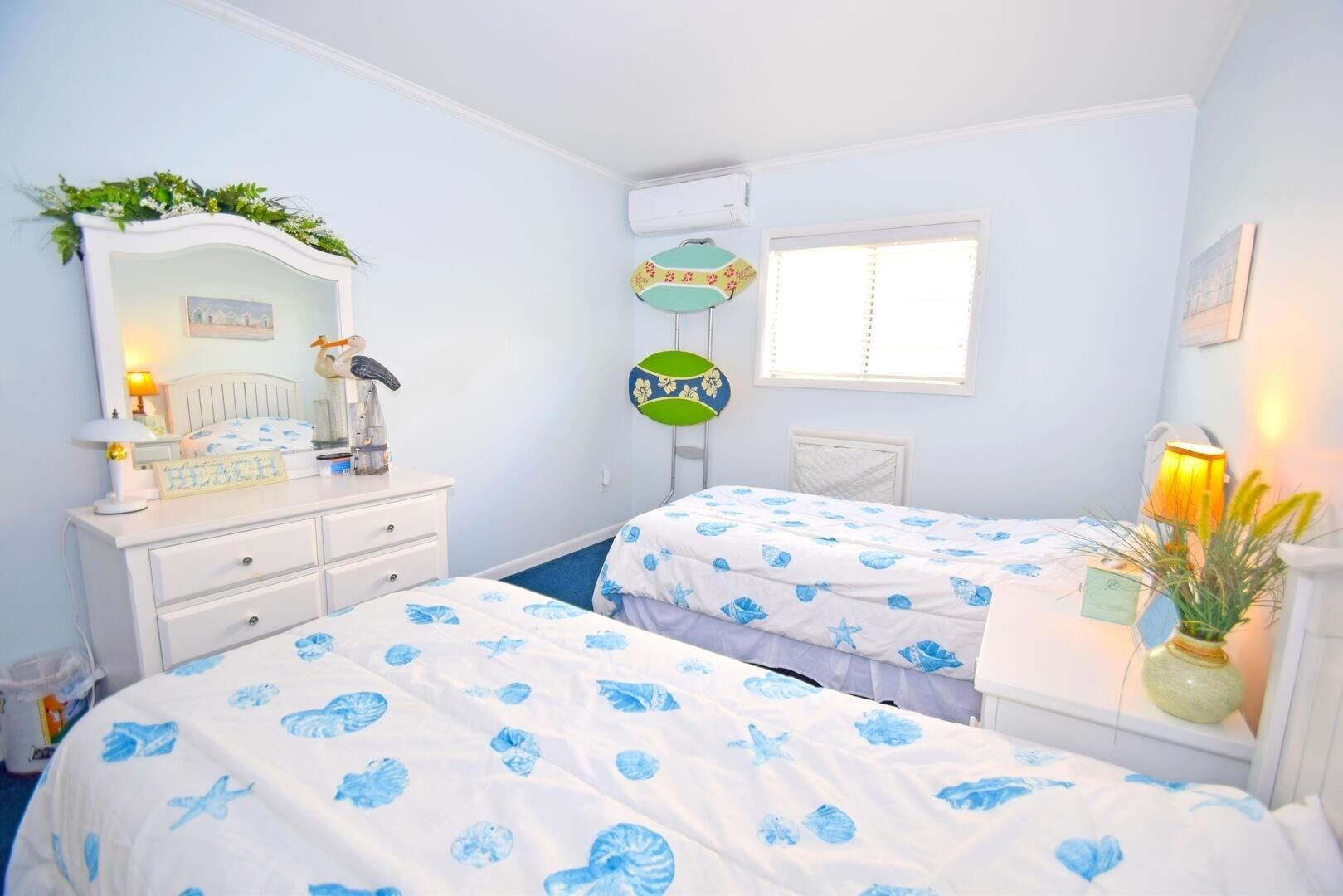 A bedroom with two beds, a dresser, a mirror, a window, and a wall-mounted air conditioning unit.