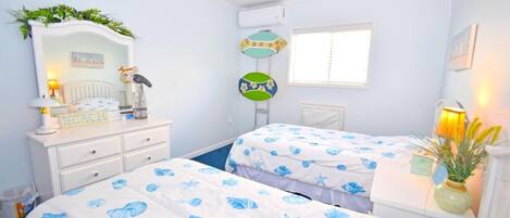 A bedroom with two beds, a dresser, a mirror, a window, and a wall-mounted air conditioning unit.