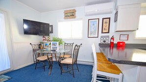 A compact kitchen with a round glass table, four chairs, a flat-screen TV, and a small island with a bar stool. - Sea Raider Iv 303 3 Bedroom Condo (Ocean City)