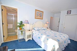 A bedroom with a bed, bedside tables, a nightstand, a lamp, a potted plant, a shower, and a door. - Sea Raider Iv 303 3 Bedroom Condo (Ocean City)