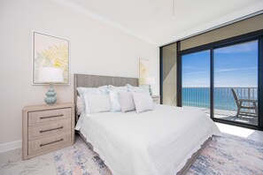 A bedroom with a large bed, a nightstand, a lamp, and a view of the ocean through a sliding glass door. - Phoenix Gulf Shores Ii 902 3 Bedroom Condo (Gulf Shores)