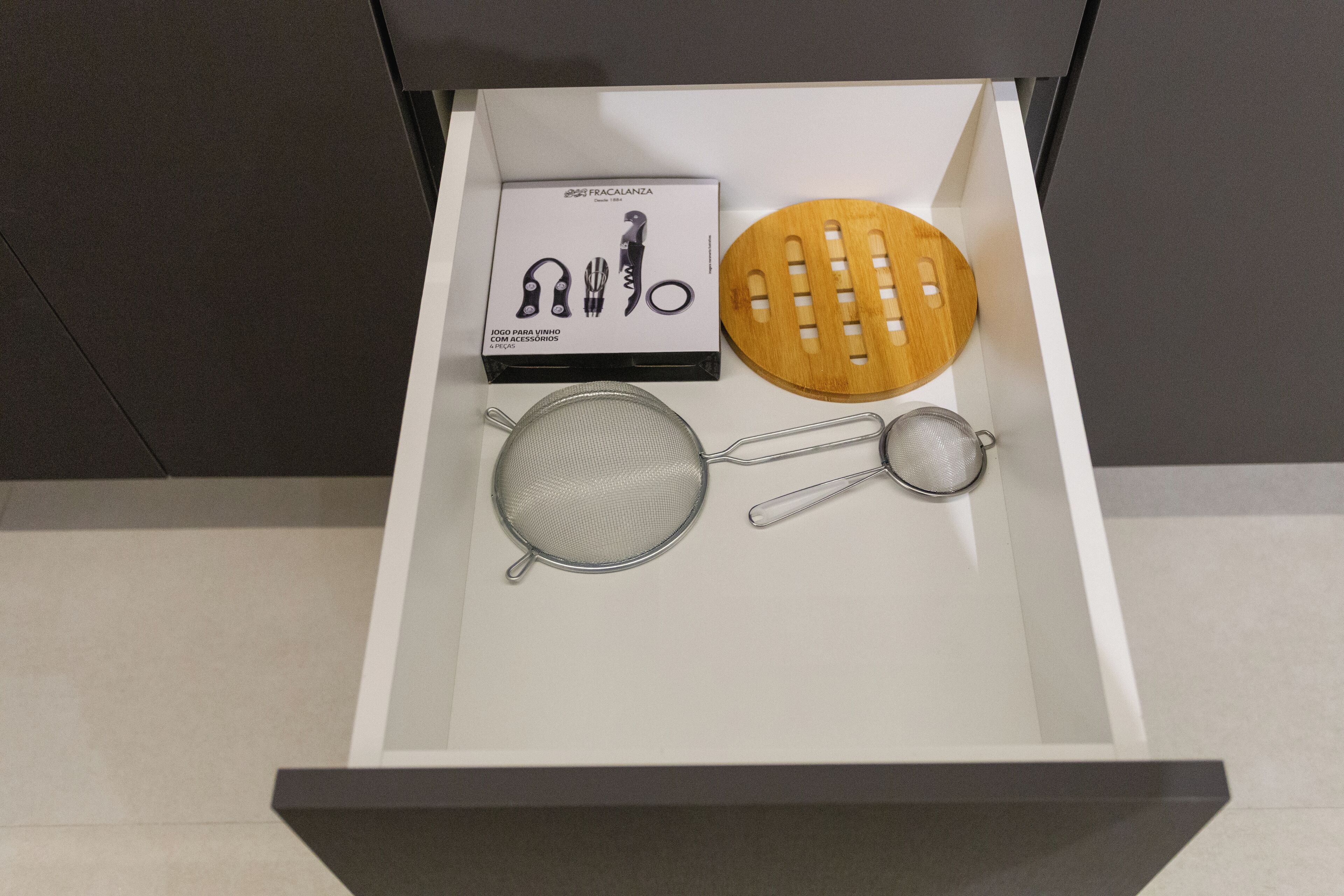 A drawer containing a wine opener, a wooden corkscrew, a mesh strainer, and a metal spoon.