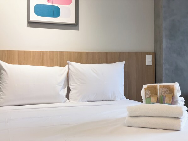 Un lit bien fait, avec du linge de lit blanc et des oreillers, un tableau abstrait encadré au-dessus, et une pile de serviettes pliées posée sur le lit.