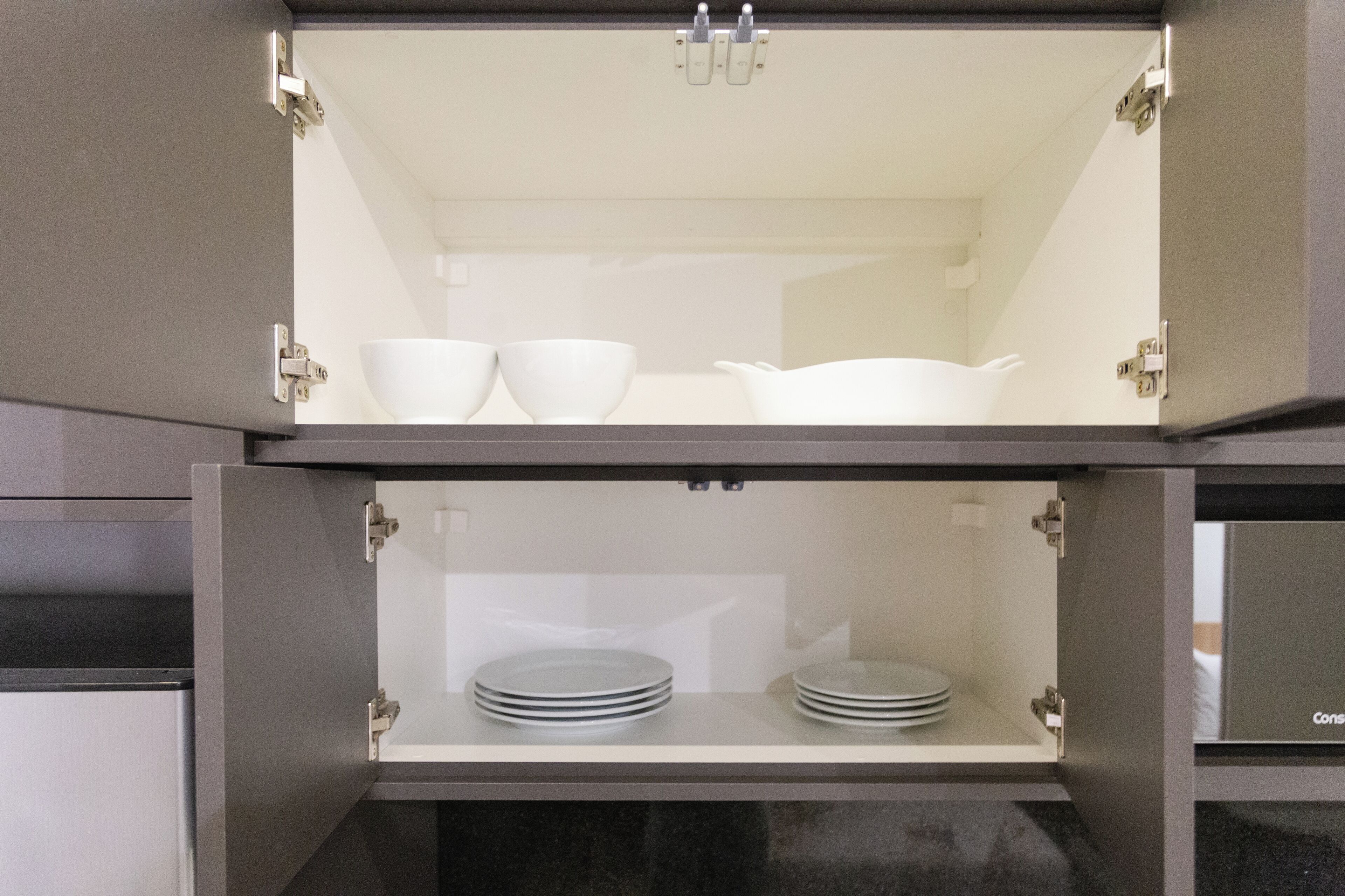 A kitchen cabinet with two shelves, each holding white bowls and plates.
