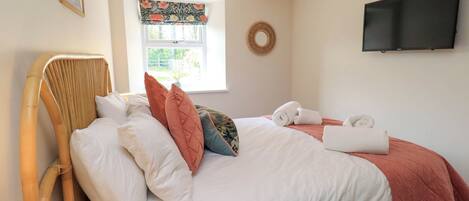 A bedroom with a bed, pillows, a chair, a television, and a window with a view.