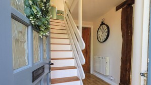 A staircase with white steps and a wooden handrail, leading to a room with a radiator and a clock on the wall.