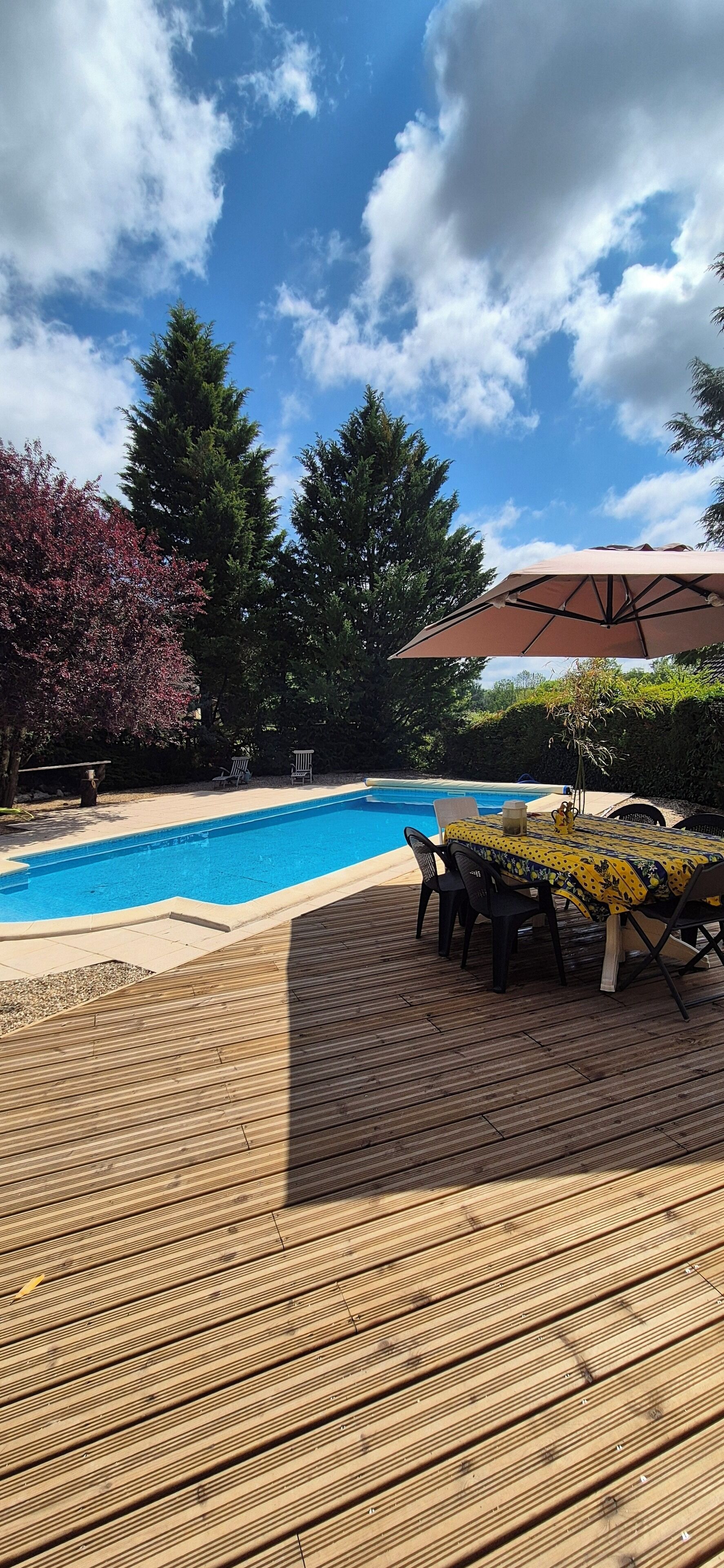 Eine Holzterrasse mit Pool, Gartenmöbeln und einem Tisch mit gelber Tischdecke.
