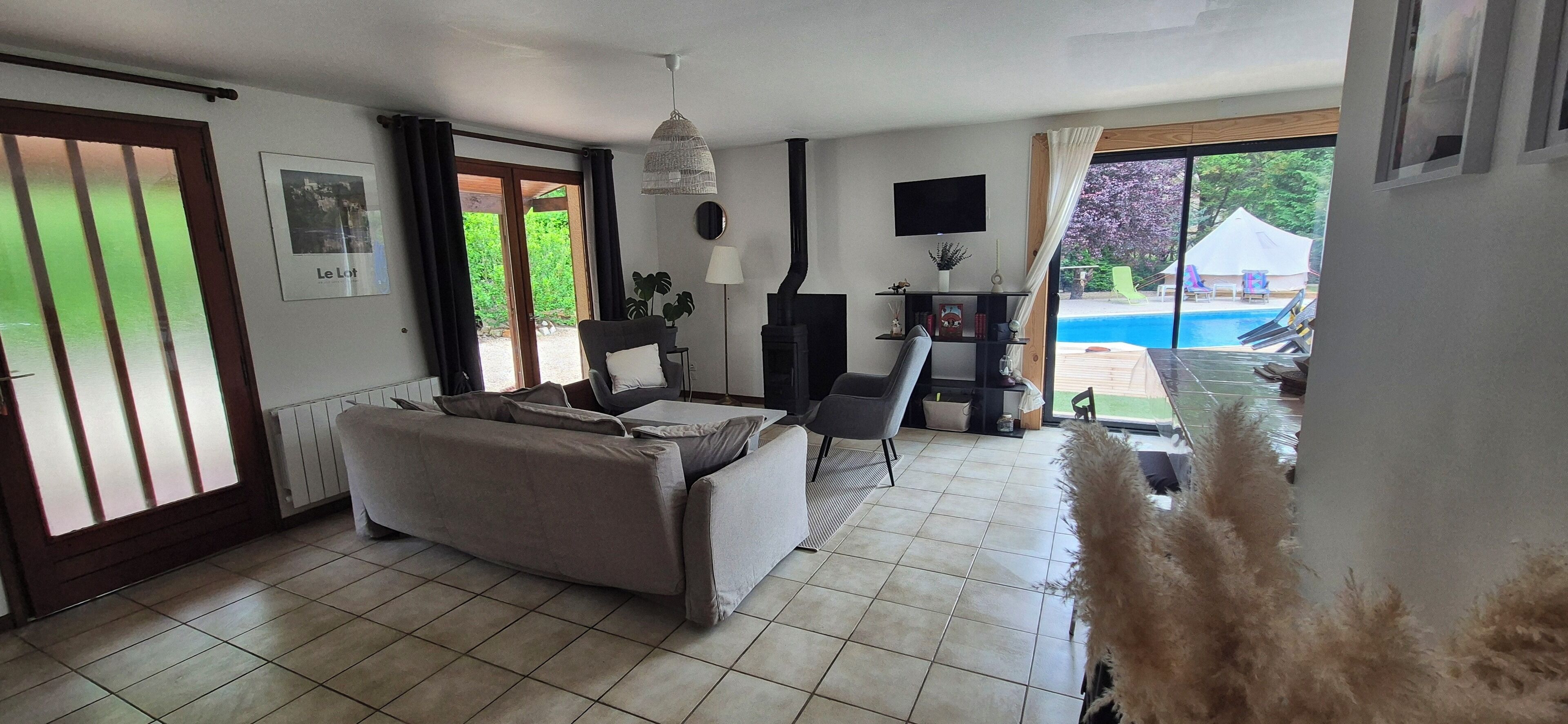 Sala de estar con sofá, televisión y chimenea. Se ve una piscina desde el interior.