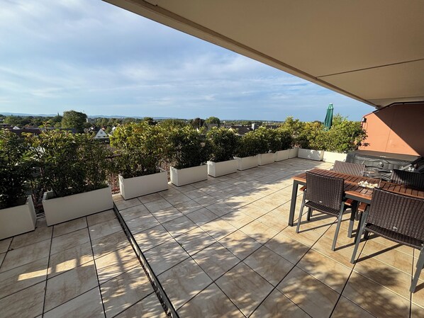 A rooftop patio with tiled flooring, outdoor furniture, and a barbecue grill.