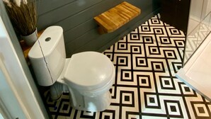 Een badkamer met een modern design, met een donkere muur, een patroon vloer, toilet, een klein houten plankje, een spiegel en een lamp.